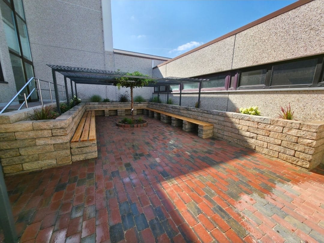 Terrasse mit rotem Klinkerpflaster, Natursteinmauer und Holzbank